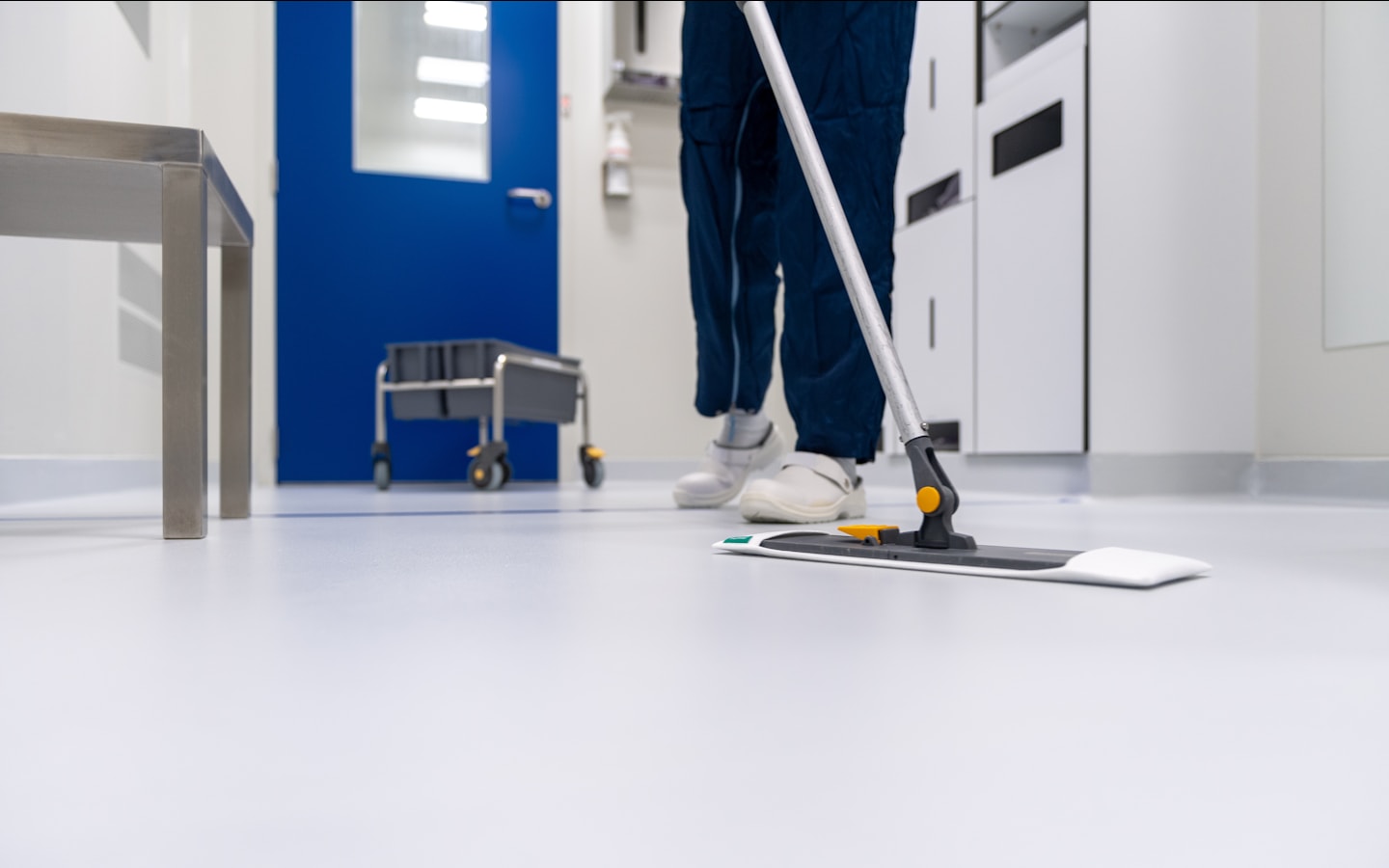 A cleaning professional mopping the floor of an institutional corridor